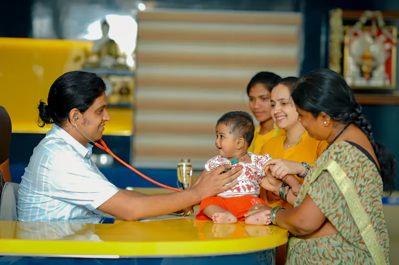 Dr. Ashok G.M. providing pediatric consultation to a smiling infant and family